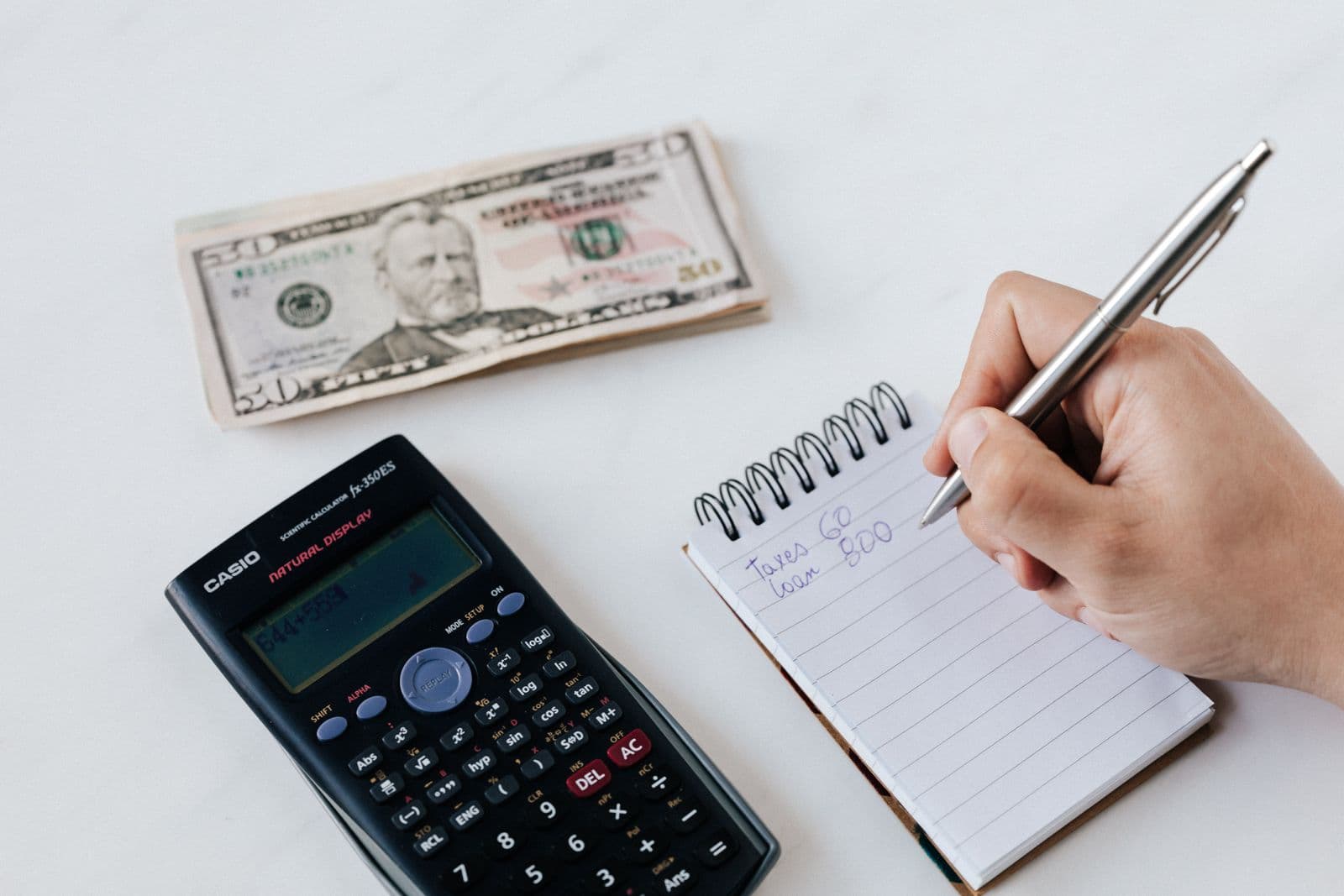 A calculator, notebook, cash, and a hand writing a household budget